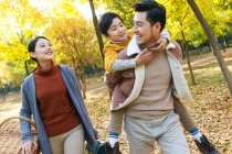 Happy asian father giving piggyback to son in autumnal park — Stock Photo