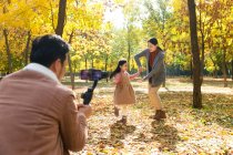 Feliz asiático padre tomando foto de hija y esposa con smartphone en el parque otoñal - foto de stock