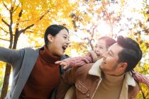 Low angle view of happy asian father giving piggyback to daughter in autumnal park — Stock Photo