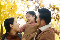 Baixo ângulo vista de feliz asiático pais e filha abraçando no outonal parque — Fotografia de Stock