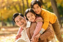 Счастливый отец с детьми развлекается в осеннем парке — стоковое фото