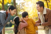 Sonrientes padres jóvenes mirando a los hermanos susurrando algo en el parque de otoño - foto de stock