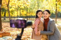 Happy asian father taking photo of daughter and wife with smartphone in autumnal park — Stock Photo