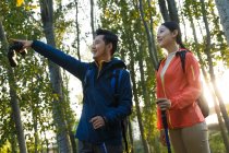 Low angle view of happy young asian couple with trekking sticks looking away in forest — Stock Photo