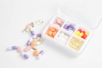 Vista ad alto angolo delle pillole nel contenitore quotidiano sulla superficie bianca — Foto stock