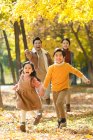 Счастливые молодые родители и милые дети, бегущие по осеннему лесу — стоковое фото