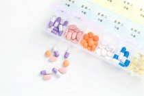 Vista superior de pílulas em recipiente diário na superfície branca — Fotografia de Stock
