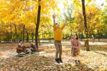 Niños felices jugando con hojas de otoño mientras los padres descansan en cuadros a cuadros en el parque - foto de stock