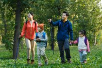 Heureux jeune asiatique famille avec sacs à dos et trekking bâtons marcher ensemble dans forêt — Photo de stock