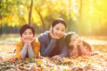 Усміхнена азіатська мати з дочкою і сином лежить на листі в автономному парку і дивиться на камеру — стокове фото