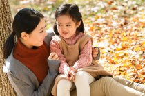 Vue grand angle de heureux asiatique mère et fille assis ensemble dans automne parc — Photo de stock