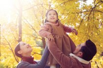 Happy asian parents lifting daughter in autumnal park — Stock Photo