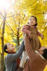 Glückliche asiatische Eltern heben Tochter in herbstlichen Park — Stockfoto