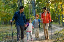 Щаслива молода сім'я з рюкзаками і палицями, що тримаються за руки і ходять разом в осінньому лісі — стокове фото