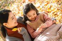 Vue grand angle de belle mère asiatique heureuse et fille jouant avec des feuilles d'automne dans le parc — Photo de stock