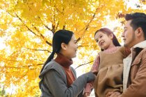 Basso angolo vista di felice asiatico genitori e figlia abbracci in autunno parco — Foto stock