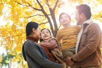 Low angle view of happy young parents carrying adorable children in autumn forest — Stock Photo