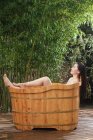 Schöne asiatische Frau liegt in hölzerner Badewanne im Garten — Stockfoto