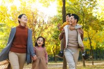 Счастливая молодая азиатская семья с корзиной для пикника, гуляющая вместе в осеннем парке — стоковое фото