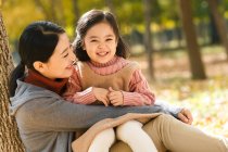 Счастливые мать и дочь сидят и обнимаются в осеннем парке — стоковое фото