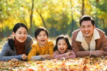Felici giovani genitori con due bambini sdraiati insieme e sorridenti alla macchina fotografica nel parco autunnale — Foto stock