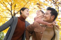 Basso angolo vista di felice asiatico padre dando a cavalluccio a figlia in autunno parco — Foto stock