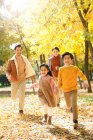 Heureux jeune asiatique famille avec deux enfants courir dans automne parc — Photo de stock