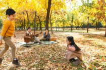 Adorable happy children playing with autumn leaves and parents enjoying guitar during picnic in forest — Stock Photo