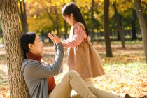Vista lateral de feliz asiático madre e hija jugando juntos en otoño parque - foto de stock