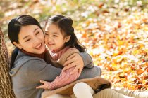 Високий кут зору щаслива азіатська мати і дочка сидять і обіймаються в осінньому парку — стокове фото