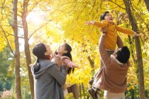 Padres jóvenes felices jugando con niños adorables en el parque de otoño - foto de stock