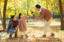 Felice padre asiatico scattare foto di figlia e moglie con smartphone nel parco autunnale — Foto stock