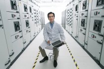 Technical personnel in white coat working with laptop computer in the voltage room — Stock Photo