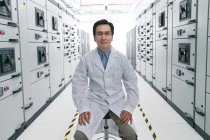 Технический персонал в лабораторном халате улыбается на камеру во время работы в комнате напряжения — стоковое фото
