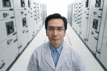 Технічний персонал в лабораторному пальто посміхається на камеру під час роботи в кімнаті напруги — стокове фото