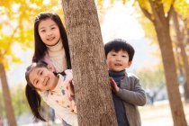 Heureux garçon et les filles debout ensemble près de l'arbre et souriant à la caméra dans le parc d'automne — Photo de stock