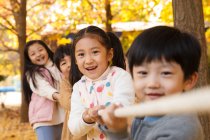 Adorable happy chinese children playing tug of war in autumn park — Stock Photo