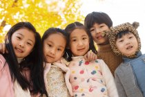 Five adorable asian kids hugging and looking at camera in autumnal park — Stock Photo