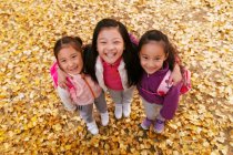 Alto ângulo vista de três adorável sorrindo asiático crianças abraçando no outonal parque e olhando para câmera — Fotografia de Stock