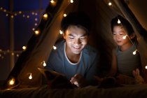 Glücklicher asiatischer Vater und Vorschulsohn schauen zu Hause im Zelt etwas auf dem Tablet — Stockfoto