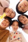 Tiefansicht von fünf entzückend lächelnden asiatischen Kindern, die im herbstlichen Park in die Kamera schauen — Stockfoto