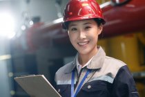 Lächelnde Technikerin mit Helm inspiziert Brandschutz in Fabrik und blickt in Kamera — Stockfoto