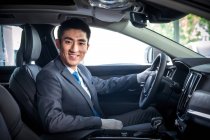 Handsome smiling asian man sitting in car and looking at camera — Stock Photo