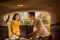 Asian couple taking stuff for picnic from car in autumnal forest — Stock Photo
