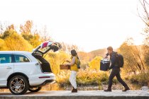 Азиатская пара берет вещи для пикника из автомобиля в осеннем лесу — стоковое фото