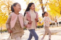 Tres adorable feliz asiático niños corriendo en otoñal parque - foto de stock