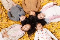 High angle view of five adorable asian kids lying on foliage in autumnal park — Stock Photo