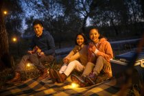 Tre amici asiatici seduti su una coperta con ukulele e guardando la fotocamera nella foresta serale autunnale — Foto stock