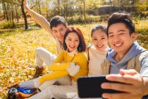 Quattro giovani sorridenti amici asiatici scattare selfie con smartphone nella foresta autunnale — Foto stock