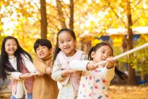 Adorable happy chinese children playing tug of war in autumn park — Stock Photo
